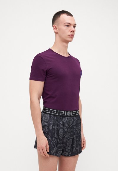 T-shirt en coton violet associé à un short noir à motifs avec une ceinture décorative. Le T-shirt a un col rond et des manches courtes.