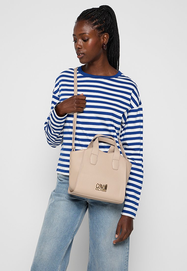 Bolso de mano de cuero beige con dos asas cortas y una correa de hombro ajustable. Presenta un logo dorado en relieve en la parte frontal.