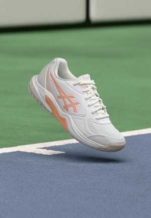 Papuc sport alb și piersică plutind deasupra unui teren de tenis cu suprafețe verzi și albastre și linii de delimitare albe.