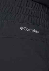 Svarta Columbia-byxor har en texturerad, elastisk midja och en signatur broderad logotyp. Tyget verkar lätt och flexibelt.