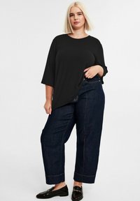 Schwarzes, geripptes T-Shirt mit weiten 3/4-Ärmeln, kombiniert mit hochtaillierten, lockeren, dunklen Denim-Jeans mit goldenen Nähten und einem umgeschlagenen Saum.
