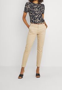 Granatowa, kwiatowa, krótko-sleeve bluzka w połączeniu z beżowymi, dopasowanymi spodniami. Strój zawiera prosty czarny pasek oraz czarne sandały na obcasie z odkrytymi palcami.