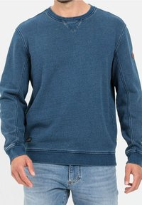 Felpa blu scuro con maniche lunghe, scollatura rotonda e dettagli di cucitura visibili. Presenta un piccolo logo sulla manica e polsini a costine.