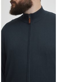 Tmavě námořnický svetr na zip s žebrovaným límcem a zipem s koženým akcentem. Texturovaný pletený materiál, bez zdobení.