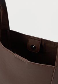 Hnedá kožená taška cez rameno s hladkým povrchom, ktorá má vnútorné zacvakávacie tlačidlo a otvorený dizajn pre jednoduchý prístup.