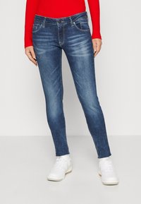 Jeans ajustados en denim azul oscuro con un acabado desgastado. Presenta un diseño clásico de cinco bolsillos, trabillas para cinturón y un cierre de botón metálico.