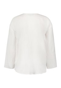 Haut en lin blanc à manches longues, coupe décontractée et encolure ronde. La texture semble légère et respirante.