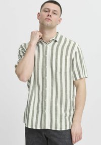 Košile s krátkým rukávem v zeleno-bílém pruhovaném provedení z lnu, s knoflíkovým zapínáním vpředu a náprsní kapsou. Měkká, strukturovaná tkanina.