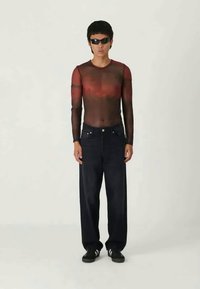 Haut transparent noir à manches longues avec des sections dégradées rouges, associé à un jean en denim noir ample et des baskets noires avec des accents blancs.