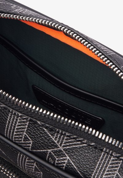 Intérieur de sac noir texturé avec doublure orange et tissu sombre. Comprend une fermeture éclair argentée et une étiquette en cuir noir. Motif géométrique à l'extérieur.