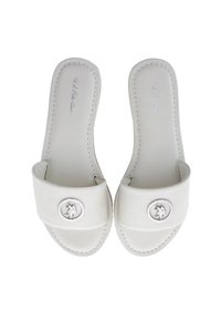 White leather slide sandals feature a wide strap with a circular silver emblem and stitching detail, offering a smooth, minimal design.
