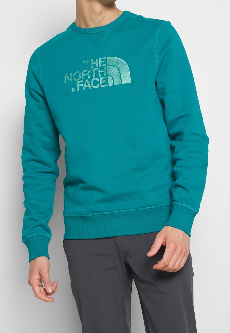Sweatshirt turquoise de The North Face, col rond, avec un grand logo argenté sur la poitrine. Mélange de coton, côtes aux poignets et à l'ourlet.