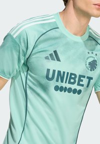 Mintgrön sporttröja med tre vita ränder på axlarna, med "UNIBET"-logotyp och F.C. Köpenhamn-emblem på framsidan. Slät textur.