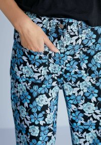 Květované kalhoty s černým pozadím, s modrými a bílými květinami. Obsahují přední kapsy a zapínání na knoflík v pase.