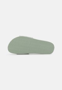 Sandal outsole in soft mint green rubber, featuring a textured wavy pattern for grip and flexibility. Rounded heel edge for comfort.