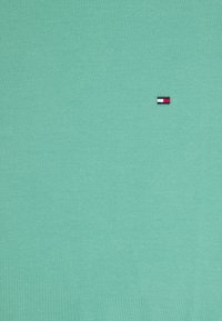 Vihreä piparmintun värinen puuvillahihaton paita, jossa on pieni brodeerattu logo punaisella, valkoisella ja sinisellä vasemmalla rinnalla. Yksinkertainen, kevyt muotoilu.