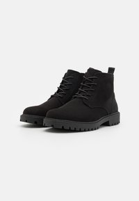 Stivaletti alla caviglia in suede nero con punta tonda, chiusura con lacci, suola in gomma testurizzata e una linguetta sul retro per facilitare l'uso.