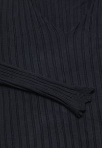 Pulover tricotat închis, cu model cu nervuri, având un guler în formă de V adânc și manșete evazate, care prezintă un model vertical de dungi uniform.