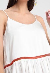 Abito bianco senza maniche con una texture morbida, caratterizzato da una striscia orizzontale rossa in vita e da una silhouette rilassata e fluida.