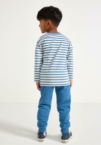 Koszula w paski z długim rękawem w kolorze niebieskim i białym, zestawiona z niebieskimi spodniami dresowymi. Strój uzupełniają trampki z białymi akcentami.