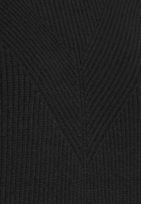 Tissu noir tricoté avec une texture côtelée formant un motif chevron symétrique et anguleux au centre.