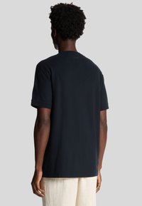 T-shirt nero a maniche corte in cotone, con collo rotondo e vestibilità rilassata, con dettagli di cucitura visibili sulle spalle e sui polsini.