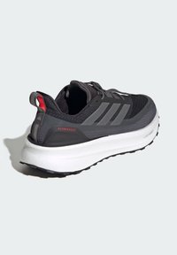 Black athletic shoe with gray accents, knitted uppers, and a white Boost midsole. Features a red pull tab and textured heel counter.