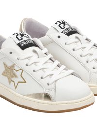 Sneaker bianche low-top con lacci bianchi, design di stelle dorate sui lati e etichette nere e bianche sulla linguetta, su una suola marrone chiaro.