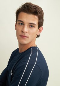 Maglietta a maniche lunghe blu navy con dettagli in piping bianco sui lati. Realizzata in un tessuto morbido, presenta un colletto a girocollo e una vestibilità comoda.