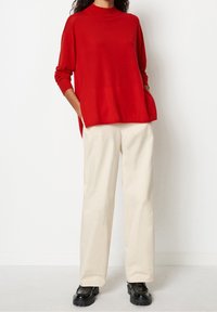 Czerwony, oversize sweter z wysokim kołnierzem, w zestawieniu z kremowymi spodniami o szerokich nogawkach i czarnymi, masywnymi butami. Prosty design, gładka faktura i luźny krój.