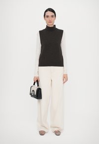Dark brown sleeveless turtleneck sweater, white long-sleeve top beneath, cream wide-leg pants, black handbag with silver accents, striped slide sandals.