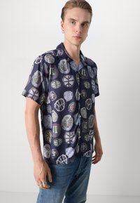 Camisa de manga curta em azul marinho escuro com um padrão circular colorido. Feita de tecido leve, apresenta um fecho de botão na frente e um corte descontraído.