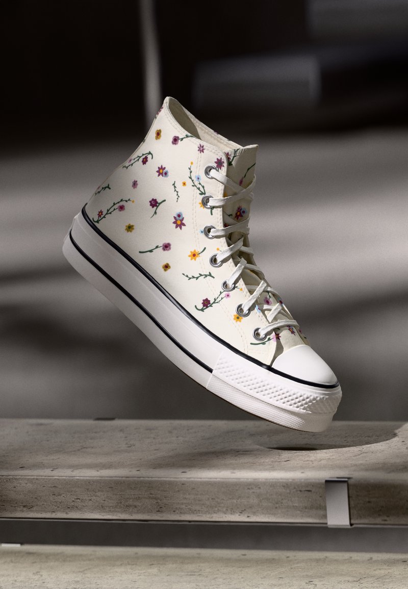 Ténis de cano alto em tecido canvas de cor creme, com bordados florais multicoloridos, sola de borracha branca e contorno em preto.
