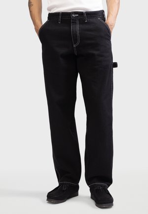Black denim pants with white stitching, featuring a straight leg design, belt loops, front pockets, and a side tab detail.