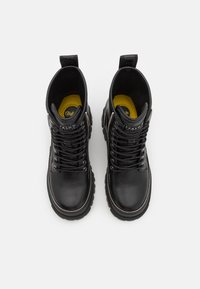 Botas de tobillo de cuero negro con un acabado texturizado, puntera redonda, herrajes en tono plateado y plantillas amarillas, con cierre de cordones y tirador.