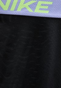 Κοντινή λήψη μαύρου υφάσματος με υφή και τρυπήματα, καθώς και μωβ λωρίδα με την επιγραφή "NIKE" με φωτεινά πράσινα γράμματα.