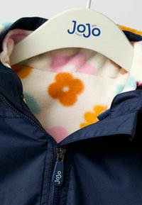Marineblau wasserfeste Jacke mit einem weichen, mehrfarbigen Blumenmuster-Fleece-Futter und einem Reißverschluss mit blauer Lasche.