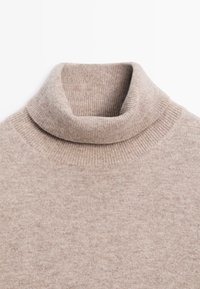 Beige rullekrave sweater lavet af blødt strikket stof, med en foldet krave og ribbet detaljering omkring halsudskæringen og skuldrene.