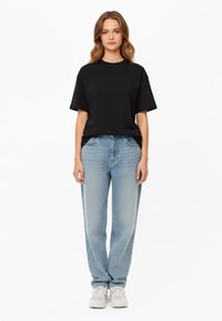 T-shirt nera a maniche corte abbinata a jeans blu chiaro a gamba dritta. Scarpe da ginnastica bianche casual completano l'outfit. Design semplice, senza motivi.