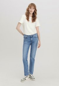 Camiseta blanca de manga corta, jeans rectos azul claro y zapatillas verdes y blancas; diseño simple con detalles mínimos.