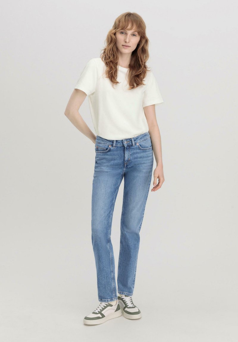 Camiseta blanca de manga corta, jeans rectos azul claro y zapatillas verdes y blancas; diseño simple con detalles mínimos.