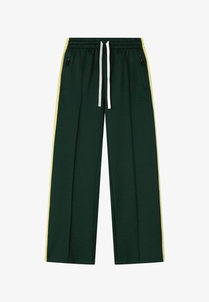 Pantaloni de trening verde închis cu dungi laterale galben deschis, talie elastică cu șnururi albe și buzunare cu fermoar pe fiecare parte.