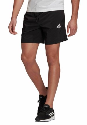 Pantaloncini sportivi neri con vita a coulisse, caratterizzati da un piccolo logo Adidas bianco sulla gamba sinistra. Indossati con scarpe da ginnastica nere.