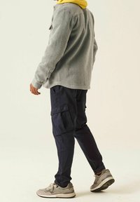 Grey corduroy button-up jacket, yellow hoodie, navy cargo pants, and gray sneakers with accents. Features ribbed texture and multiple pockets.