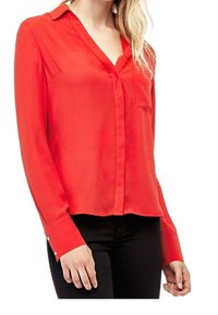 Blouse rouge à manches longues en tissu lisse, avec un col en V et une poche avant. Présente des boutons aux poignets.