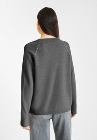 Szary sweter dziany o luźnym kroju, z wyraźnymi przeszyciami wzdłuż szwów raglanowych i ściągaczem na dole. Casualowy design.