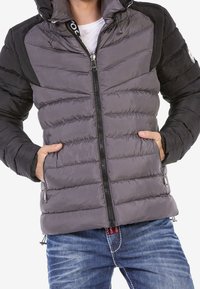 Chaqueta puffer gris con acentos negros, diseño acolchado, cierre frontal de cremallera y bolsillos. Con capucha y cordones ajustables.