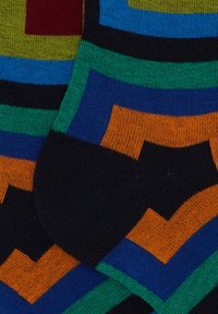 Calzini multicolori con motivi geometrici in verde, blu, arancione e nero. Realizzati in morbido materiale a maglia, con una finitura testurizzata.