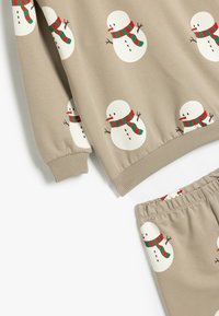 Beige sæt i sweats med hvide snemandsgrafikker, der har røde og grønne tørklæder. Ribbet afslutning ved håndled og talje. Blødt, struktureret stof.