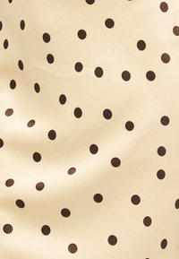 Μπεζ ύφασμα με ομοιόμορφα κατανεμημένες μικρές μαύρες πουά που δημιουργούν ένα κλασικό πουά μοτίβο με ελαφριές πτυχώσεις στο ύφασμα.